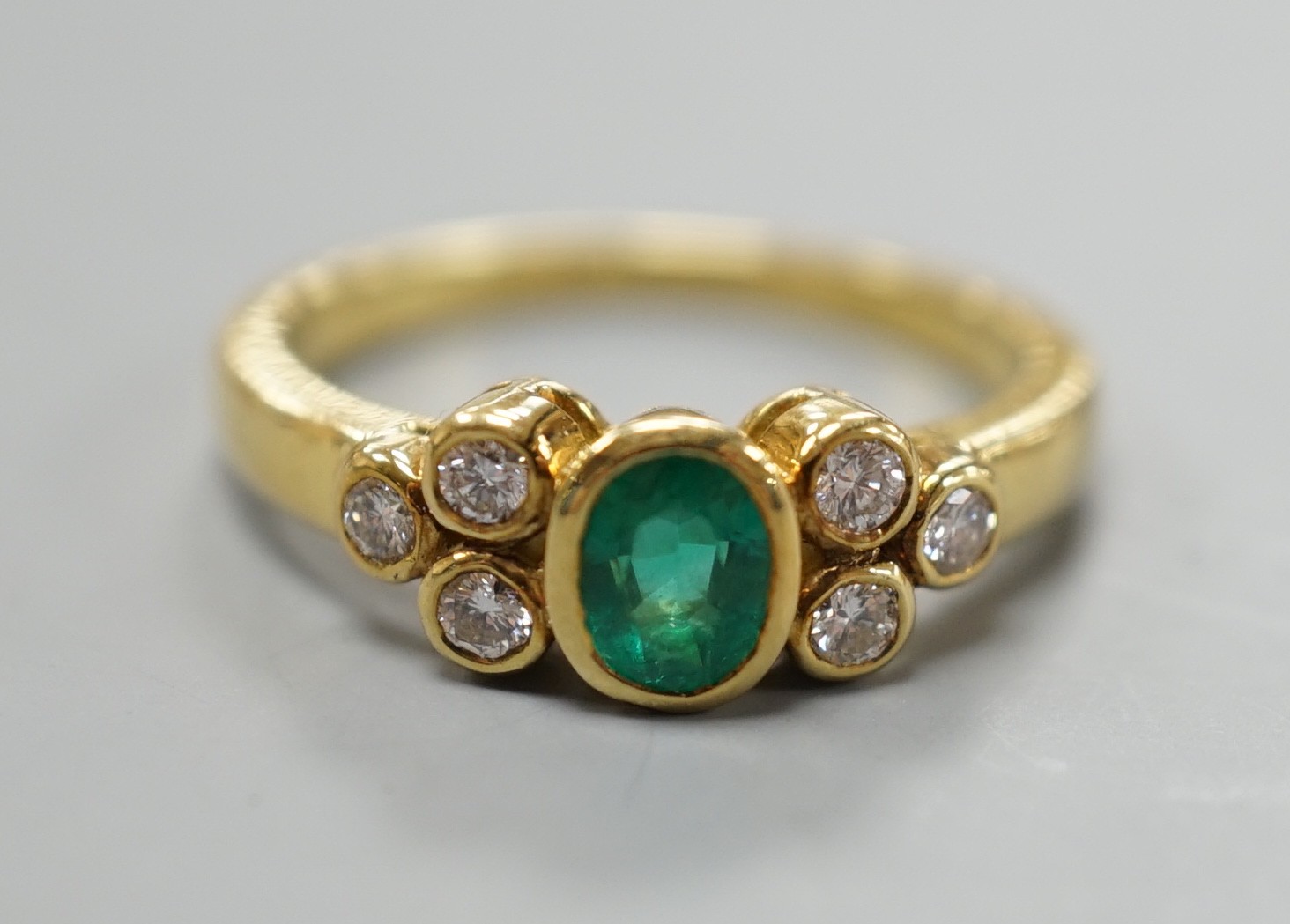 A modern yellow metal and collet set oval cut emerald ring, with six stone diamond set shoulders, size L/M, gross weight 4.1 grams.